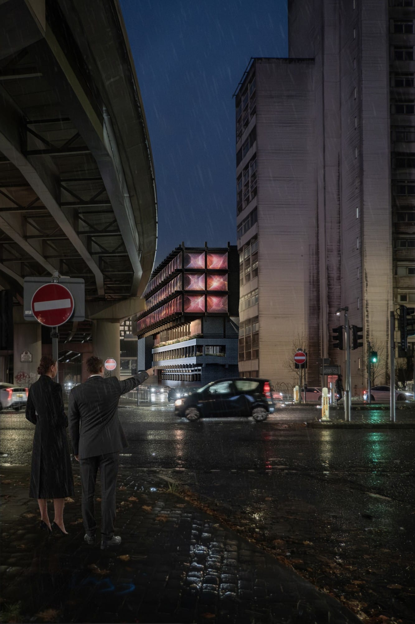 Rainy night street under the Mancunian Way flyover, with a couple pointing towards the building's facade glowing with projections between concrete towers.