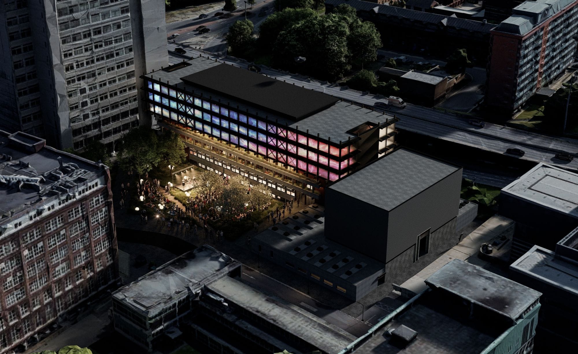 Night aerial view of the building with its ETFE facade lit in blue and pink projections above a crowded courtyard gathered around an outdoor stage.