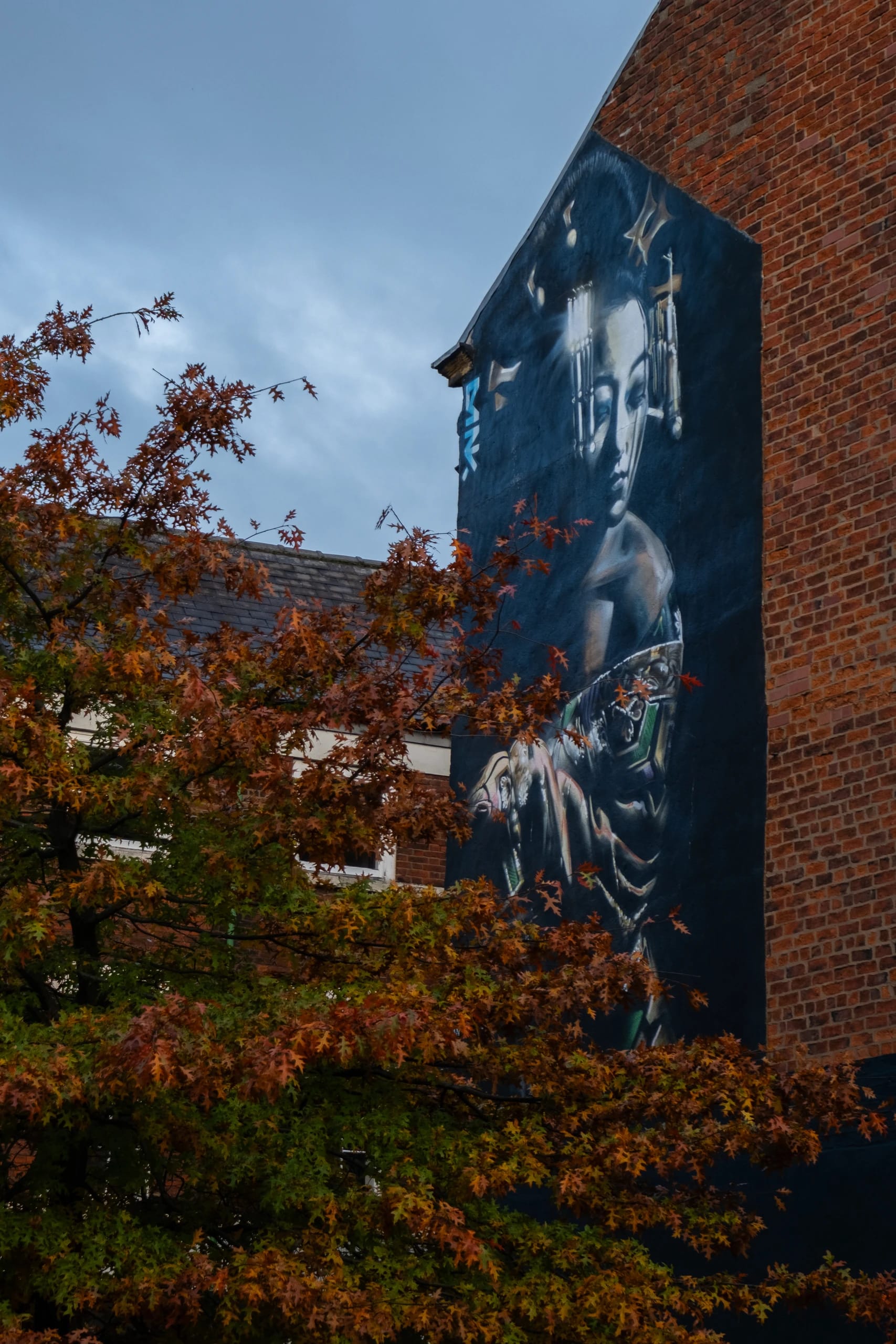 A mural on a brick wall framed by autumn foliage