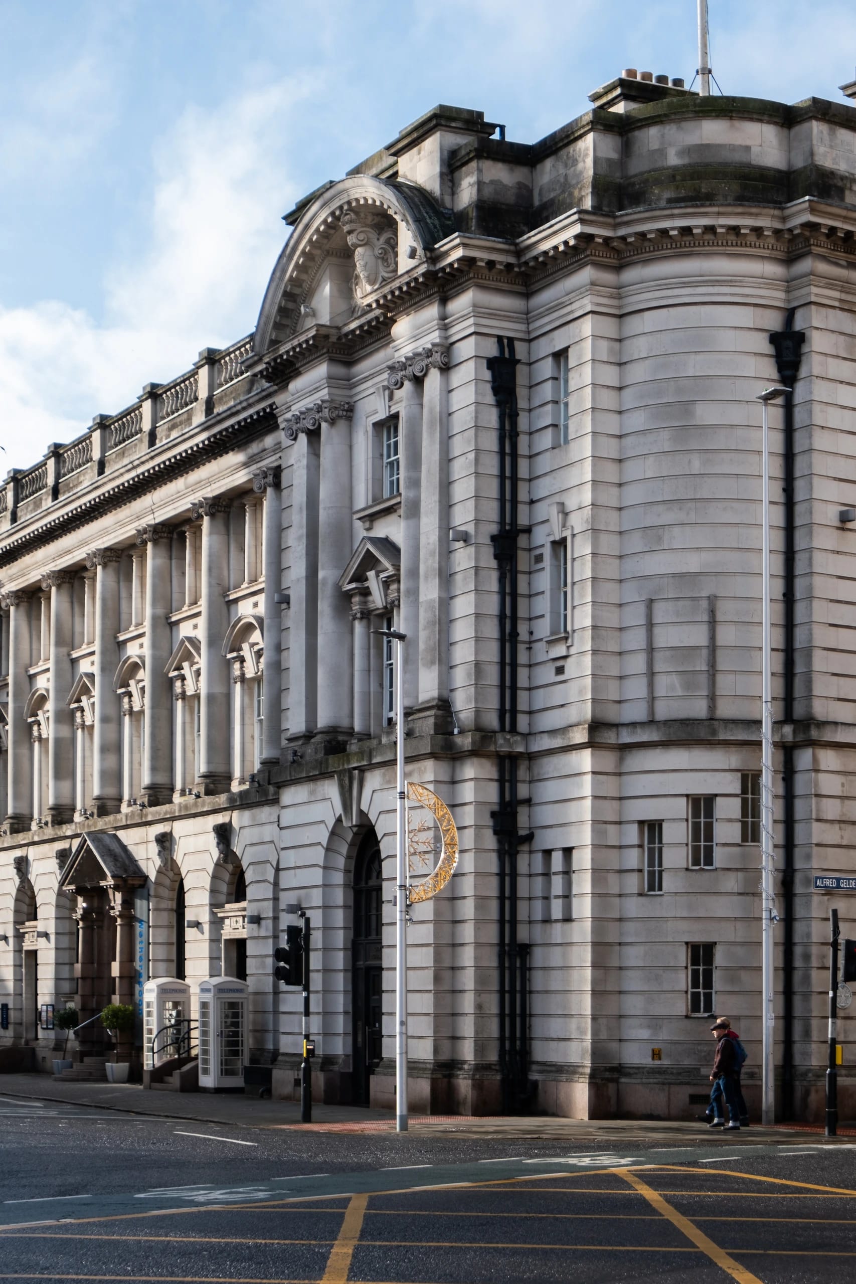 A monumental stone facade with columns and a pedestrian on the pavement